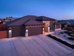 View of front facade with a garage, stone siding, concrete driveway, and stucco siding