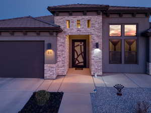 Entrance to property with an attached garage, a tiled roof, stucco siding, and driveway