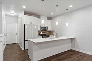 Kitchen featuring white cabinetry, stainless steel appliances, decorative backsplash, dark wood-style floors, and hanging light fixtures