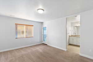 Unfurnished bedroom with light carpet, access to exterior, a textured ceiling, and connected bathroom