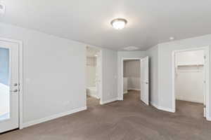 Unfurnished bedroom with carpet flooring, a spacious closet, ensuite bath, and a textured ceiling
