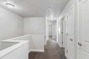 Hallway with dark carpet, an upstairs landing, and a textured ceiling