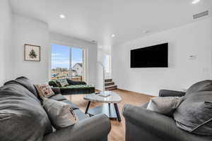 Living room with light wood finished floors, recessed lighting, and stairs