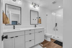 Full bathroom with dark wood-style floors, double vanity, a shower stall, and recessed lighting