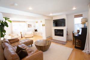 Living area with light wood-type flooring, a glass covered fireplace, and recessed lighting