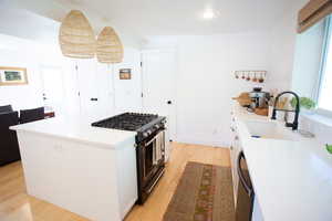 Kitchen with black appliances, hanging light fixtures, white cabinetry, light wood-style floors, and a kitchen island
