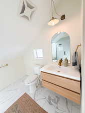 Bathroom featuring lofted ceiling, vanity, and light marble finish flooring