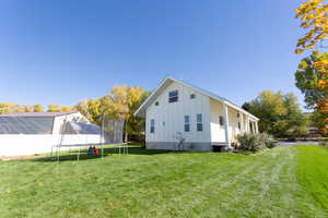 View of side of home featuring board and batten siding, a trampoline, and a yard