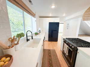 Kitchen with black appliances, white cabinetry, light wood-type flooring, light stone countertops, and recessed lighting