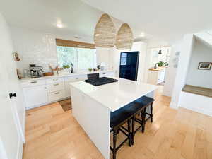 Kitchen with white cabinetry, a breakfast bar area, light wood-type flooring, a kitchen island, and recessed lighting