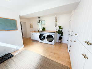 Washroom featuring light wood finished floors, washing machine and dryer, and cabinet space