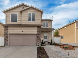 View of front of property featuring concrete driveway, stone siding, a garage, and a garden