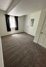 Unfurnished bedroom featuring dark colored carpet, a textured ceiling, and electric panel