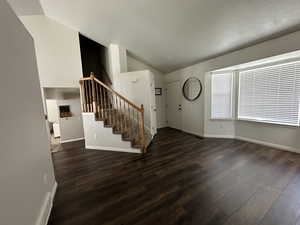 Foyer featuring dark wood-type flooring, stairs, and vaulted ceiling