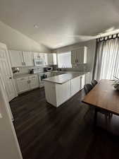 Kitchen featuring vaulted ceiling, light countertops, white cabinetry, white appliances, and dark wood finished floors