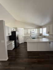 Kitchen featuring vaulted ceiling, white cabinetry, light countertops, white appliances, and a peninsula
