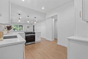Kitchen featuring range with gas stovetop, white cabinetry, light stone counters, light wood-style flooring, and hanging light fixtures