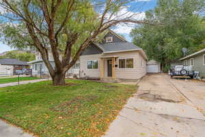 Bungalow with a front yard, a shingled roof, a detached garage, and an outbuilding