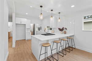 Kitchen featuring a breakfast bar area, a peninsula, backsplash, light stone counters, and white cabinetry