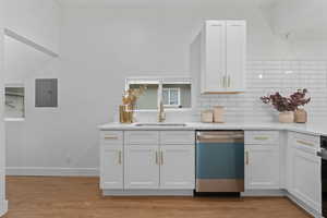 Kitchen with white cabinets, dishwashing machine, backsplash, light wood-style floors, and electric panel