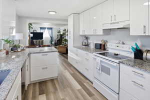 Kitchen featuring white range with electric cooktop, white cabinets, light stone countertops, and open floor plan