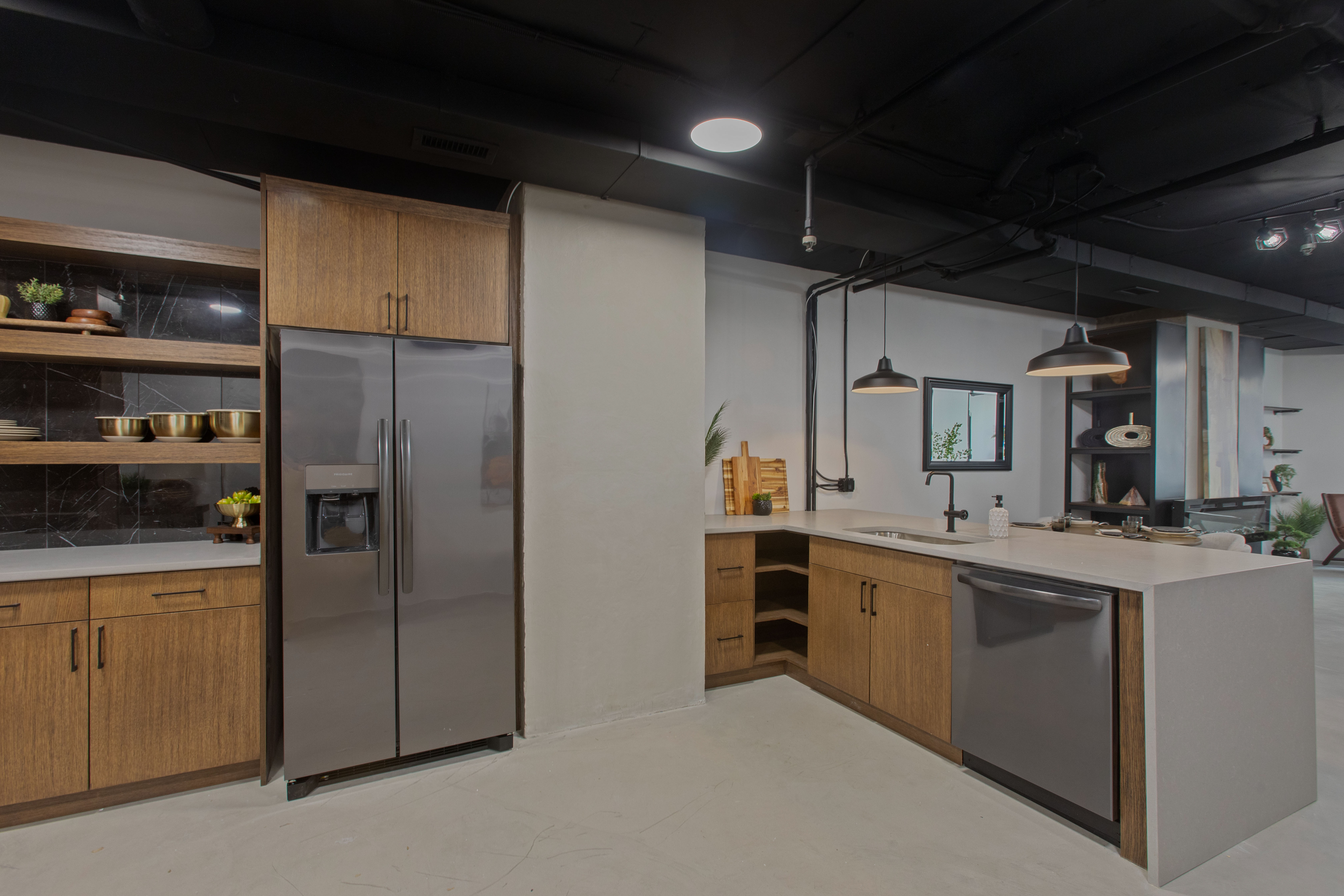 Kitchen with appliances with stainless steel finishes, a peninsula, brown cabinetry, hanging light fixtures, and light stone counters