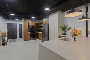 Kitchen with stainless steel appliances, open shelves, hanging light fixtures, light stone counters, and brown cabinetry