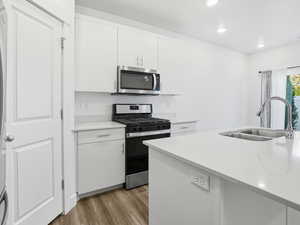 Kitchen with appliances with stainless steel finishes, white cabinets, light wood-style flooring, a center island with sink, and recessed lighting
