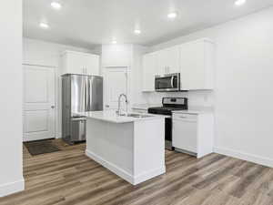 Kitchen with appliances with stainless steel finishes, light wood-type flooring, a center island with sink, white cabinets, and recessed lighting