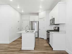 Kitchen featuring appliances with stainless steel finishes, a center island with sink, white cabinetry, light wood-type flooring, and recessed lighting