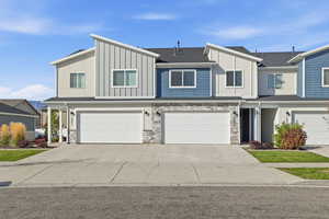 View of front of property with board and batten siding, stone siding, driveway, and a garage