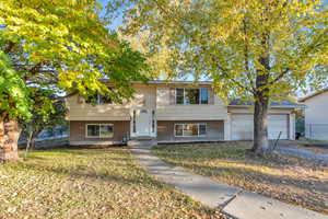 Bi-level home with brick siding, a garage, a front yard, and driveway