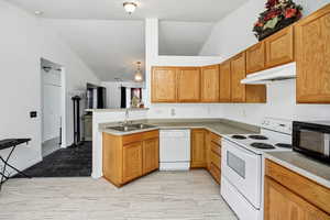 Kitchen with white appliances, lofted ceiling, light wood-style floors, under cabinet range hood, and a peninsula
