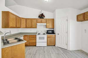Kitchen featuring white electric stove, brown cabinets, black microwave, light countertops, and lofted ceiling