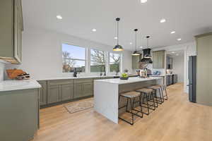 Kitchen featuring light stone countertops, a breakfast bar, hanging light fixtures, light wood-type flooring, and a center island