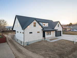 Modern farmhouse style home featuring stone siding, driveway, a standing seam roof, covered porch, and a garage