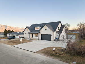 Modern farmhouse style home with stone siding, driveway, covered porch, and an attached garage