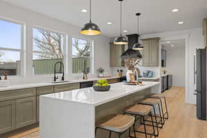 Kitchen with light stone countertops, a kitchen island, a breakfast bar area, black appliances, and gray cabinetry