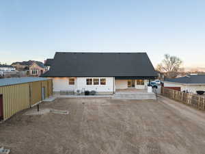 Back of property at dusk featuring a patio area, roof with shingles, and a residential view