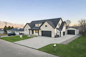 Modern farmhouse style home featuring stone siding, a porch, a lawn, and concrete driveway. The landscaping view and the secondary garage are AI-generated.