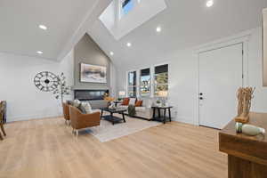 Living room with vaulted ceiling, light wood-style flooring, a glass covered fireplace, and recessed lighting