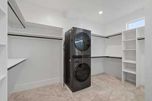 Walk-in Master closet with light carpet and stacked washer / dryer