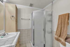 Full bath with double vanity, crown molding, tile walls, light tile patterned floors, and a shower stall