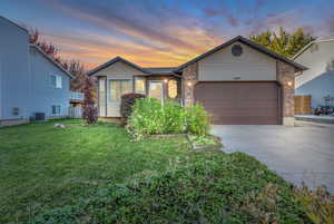 Single story home featuring driveway, brick siding, a garage, and a front yard