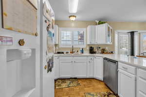Kitchen with white cabinetry, stainless steel dishwasher, glass insert cabinets, light stone counters, and a textured ceiling