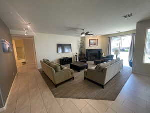 Tiled living room featuring a ceiling fan, a fireplace, and a textured ceiling