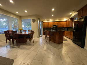 Kitchen with black appliances, recessed lighting, a breakfast bar, a kitchen island with sink, and brown cabinets