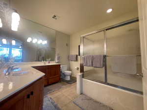 Master bathroom featuring two vanities, bath / shower combo with glass door, and light tile patterned flooring