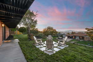 Yard at dusk featuring a fenced backyard, a patio, and a fire pit