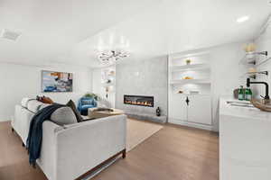 Living area with a tiled fireplace, light wood-style floors, and built in features